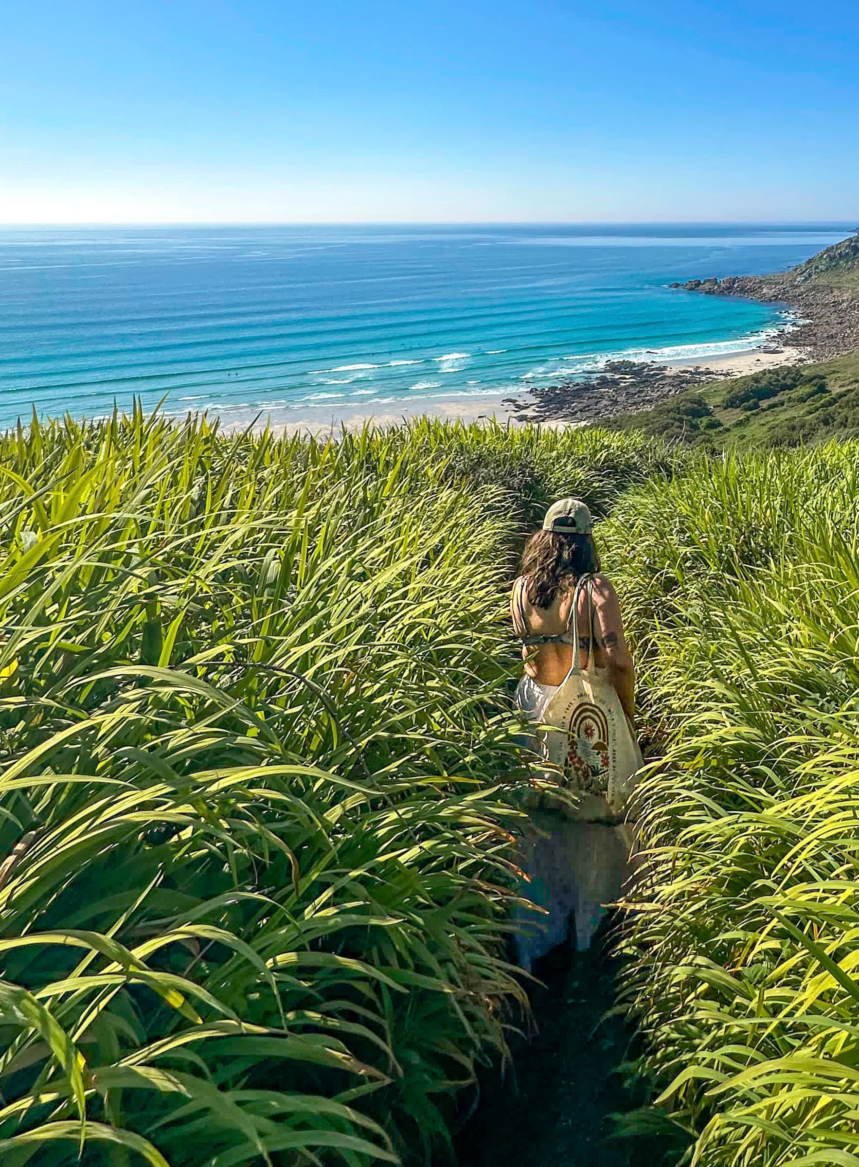 A woman walking through tall grass toward a coastal view