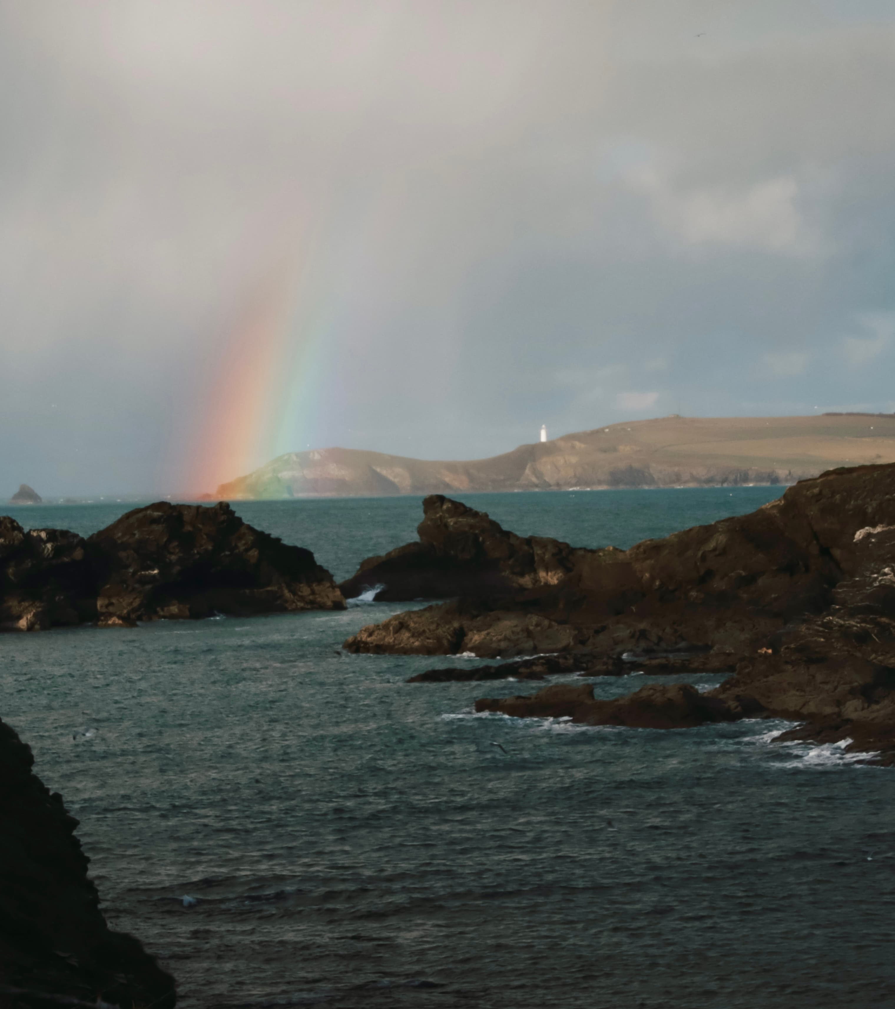 A rainbow over Pentire Headland, lighthouse in the distance