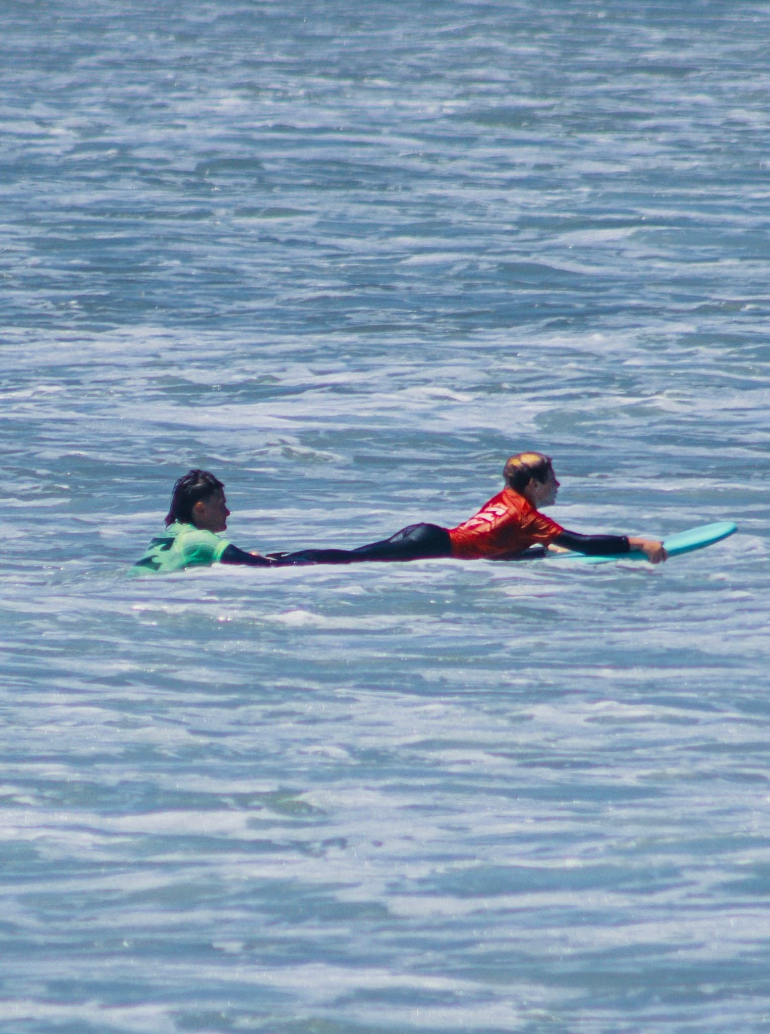 Two surfers lying flat on their boards, paddling out together