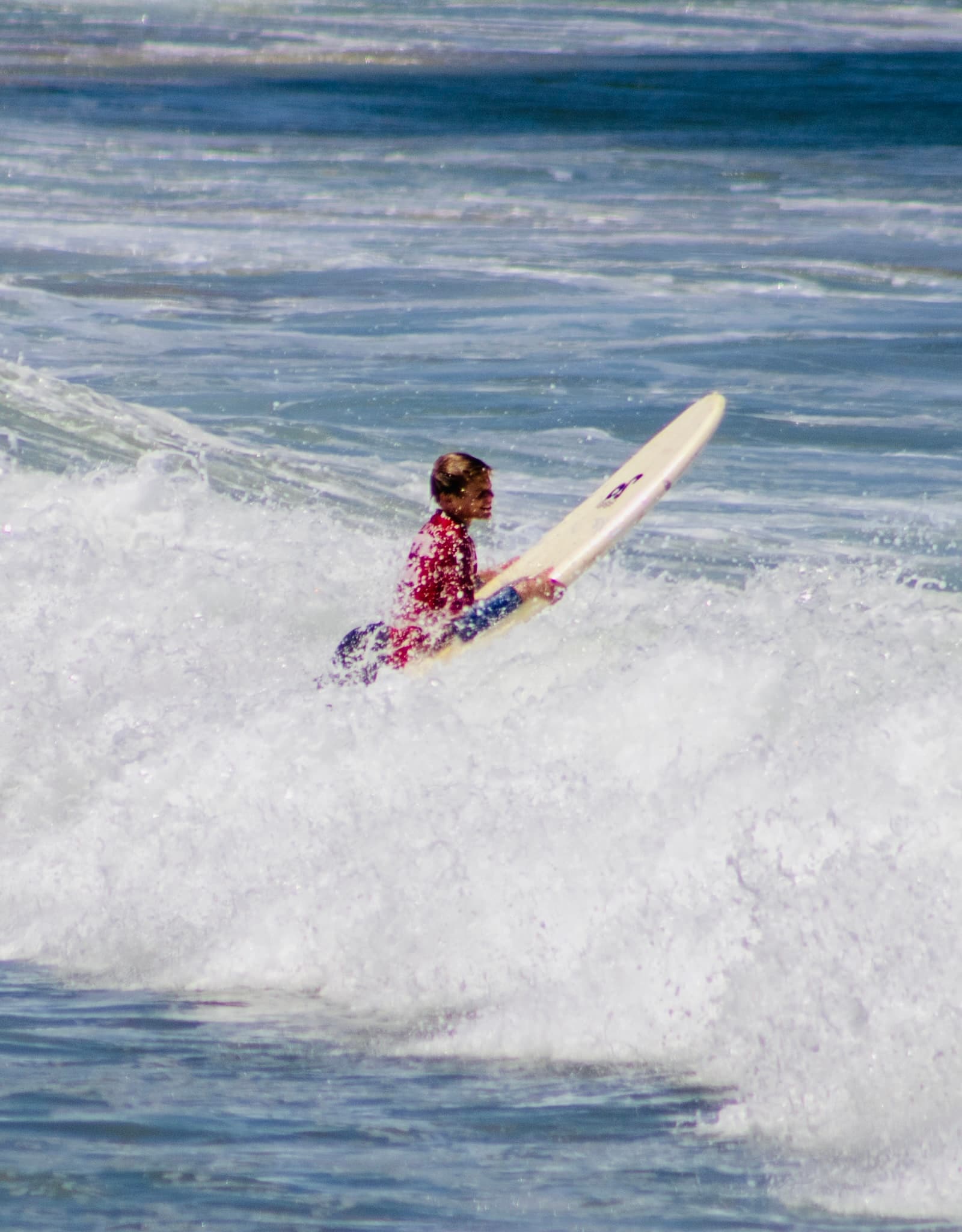 A surfer rinsing off under an outdoor shower, surfboard in hand