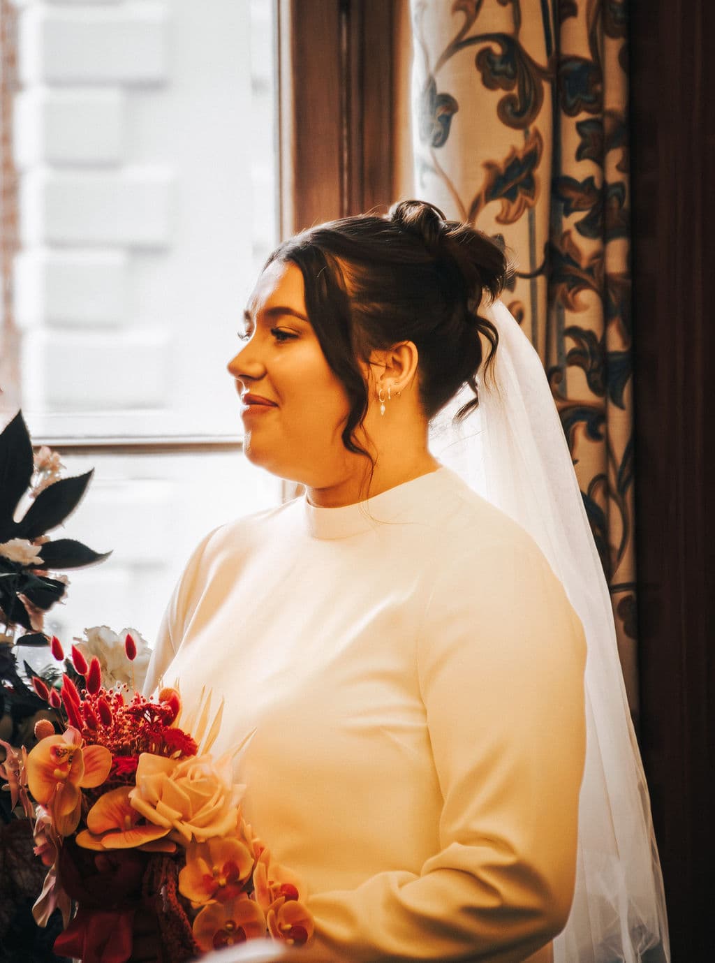 The bride by a window, veil and bouquet in soft light