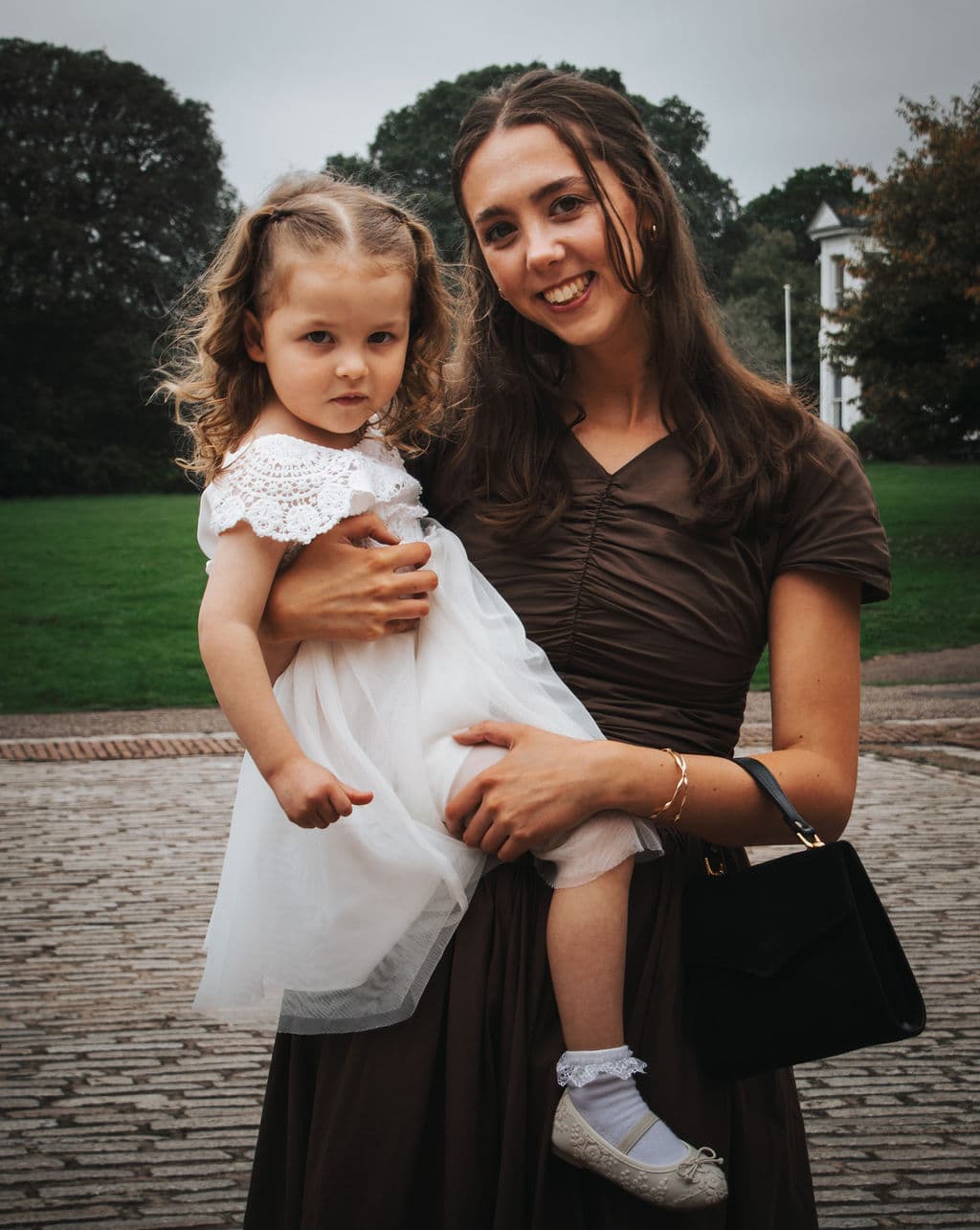 A bridesmaid holding a flower girl, both looking at the camera