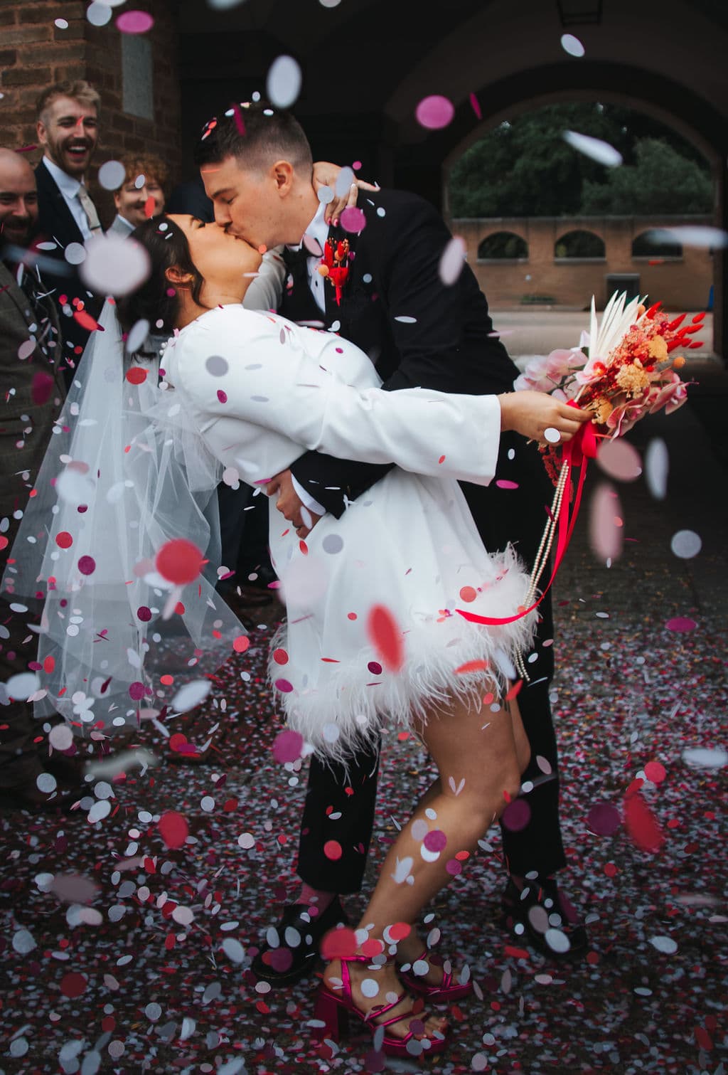 The couple kissing in a shower of confetti, groomsmen smiling behind them