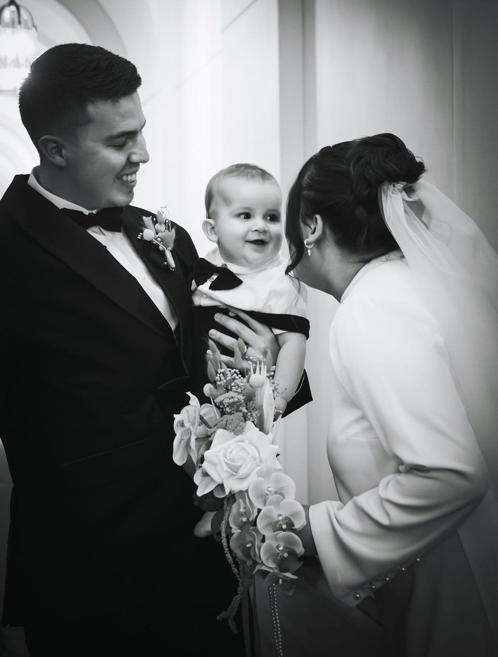 The groom and bride smiling at a baby held between them