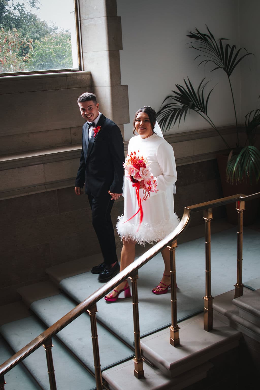 The newly married couple walking down a grand staircase, both smiling