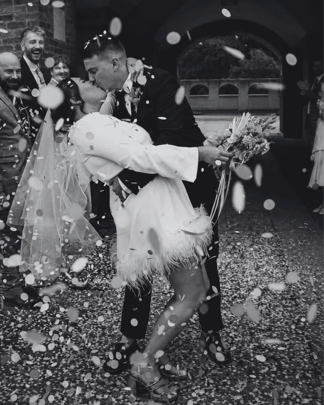 A couple kissing in a shower of confetti outside a brick archway
