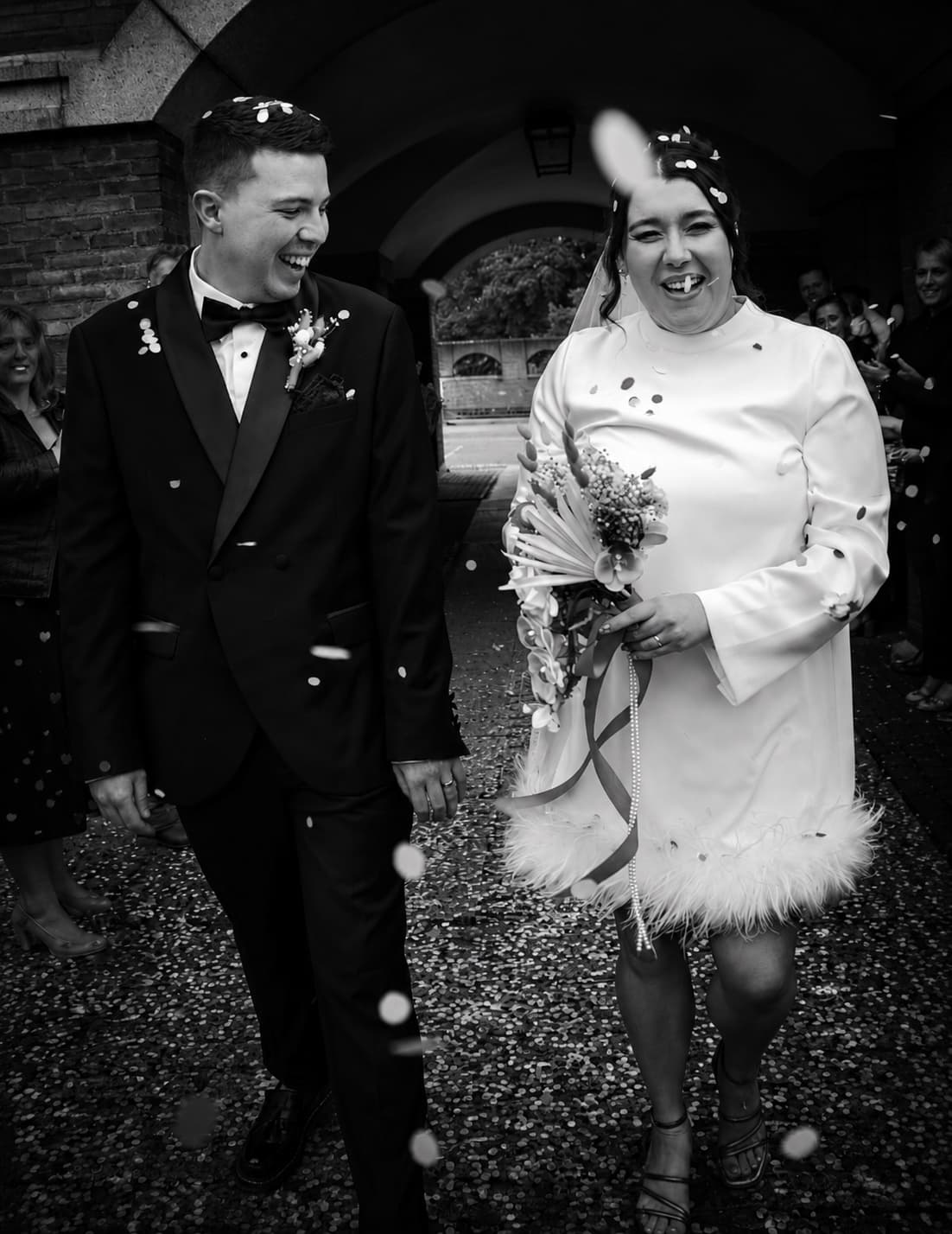 A couple walking out into a shower of confetti, both laughing