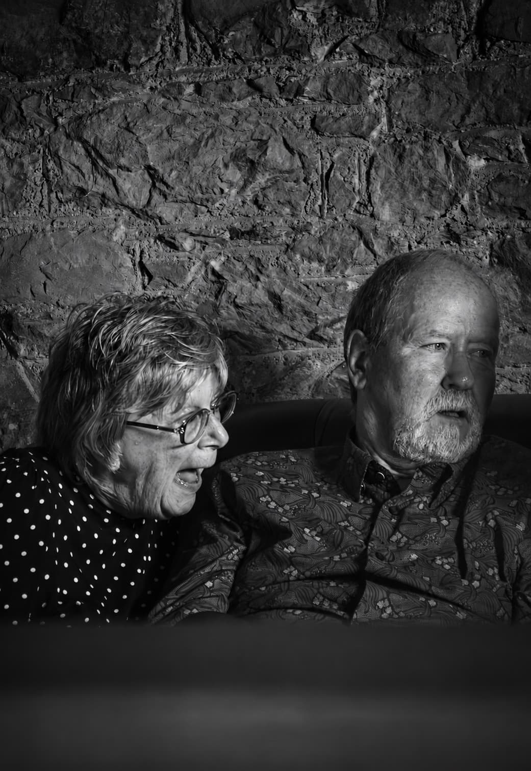 Two guests against a stone wall — the woman laughing, the man watching
