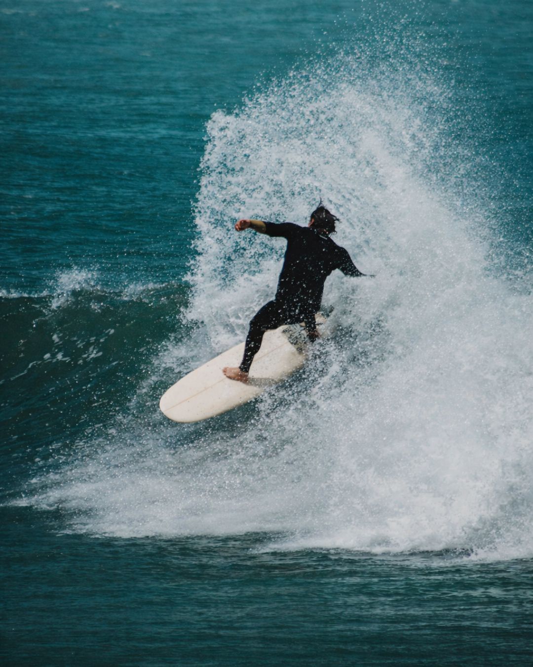 Cuan mid-turn on surfboard, spray exploding behind, teal-green Atlantic ocean