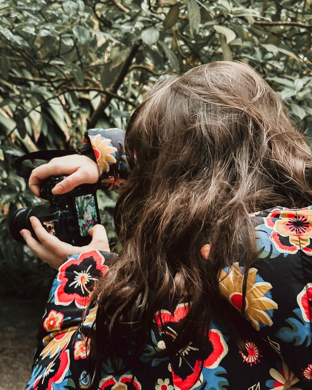 Georgia photographing through camera lens, back to camera, floral jacket, lush green foliage, South Africa