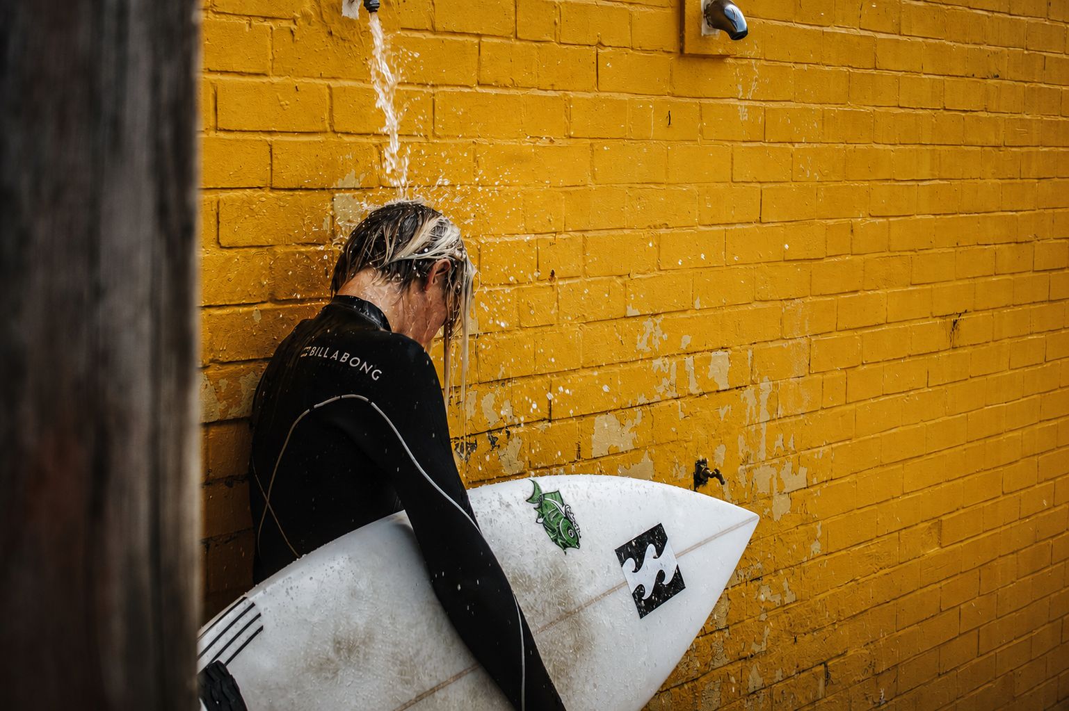 Surfer rinsing off at yellow brick wall post-session