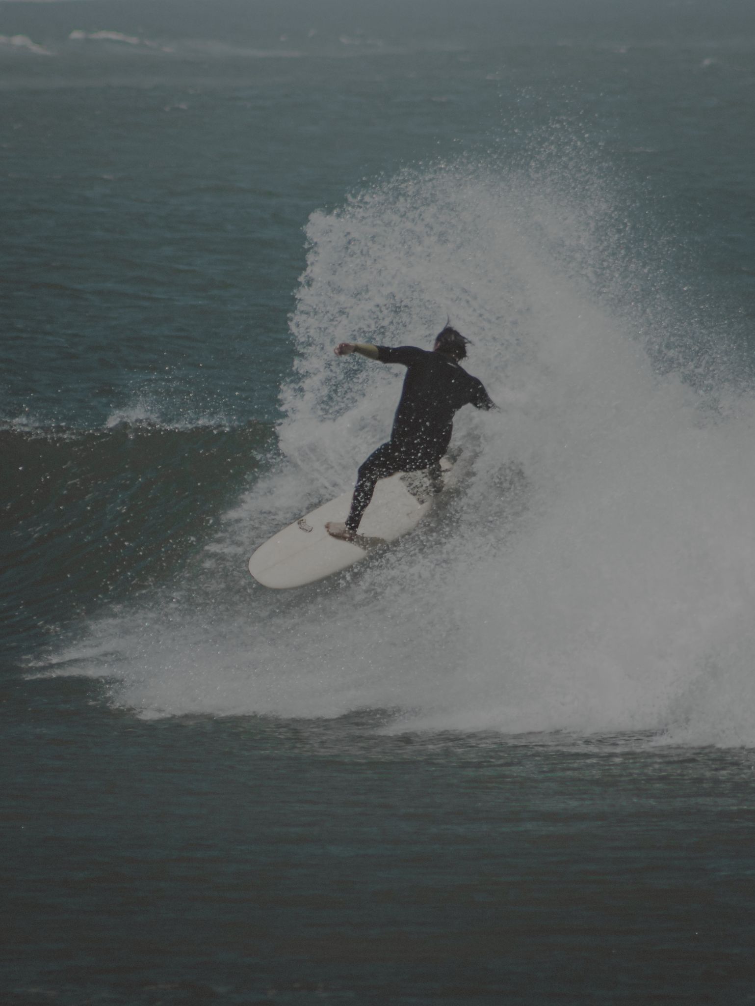 Young surfer close-up with spray, face visible, joy, Cornish pier background